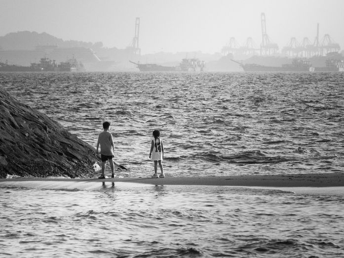 Two children walking along a shoreline with ships in the distance, representing reflection on life, circumstance, and the grace that shapes the path we inhabit.