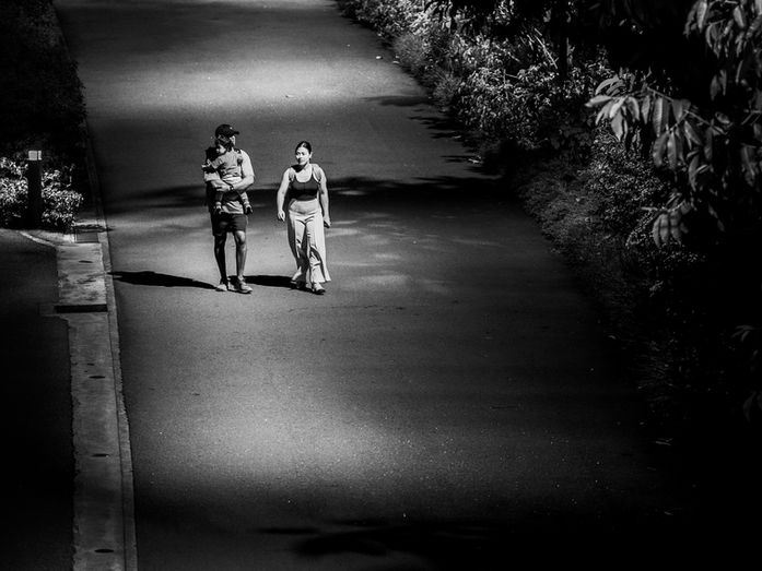 Black and white photograph of two adults walking along a long road while one carries a child, representing freedom, responsibility, and the quiet choices that shape a life.