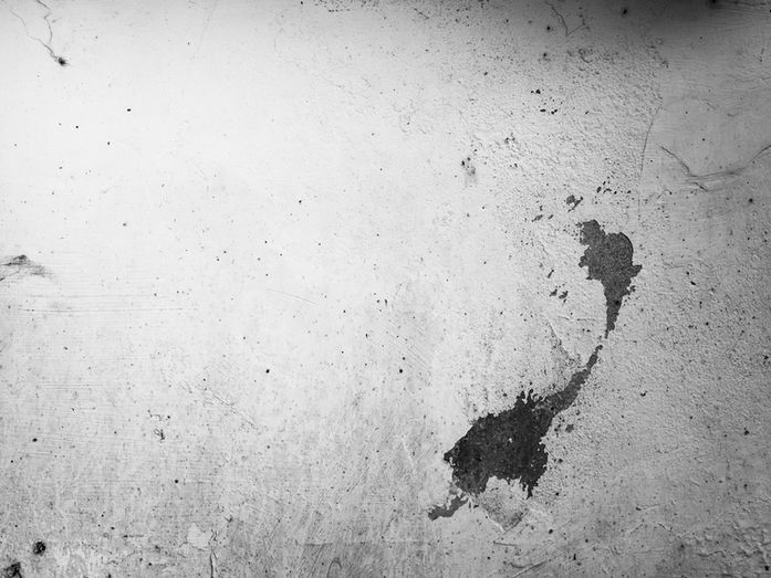 A damaged wall surface with a visible hole, photographed in black and white.