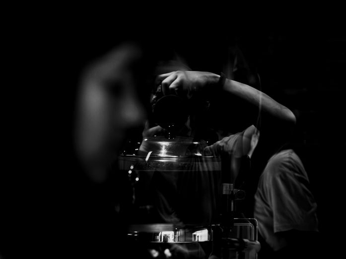 Black and white urban reflection photography featuring Gary PWK holding a camera, layered reflections, and a blurred subject entering the frame, representing fragmented perception and quiet observation.