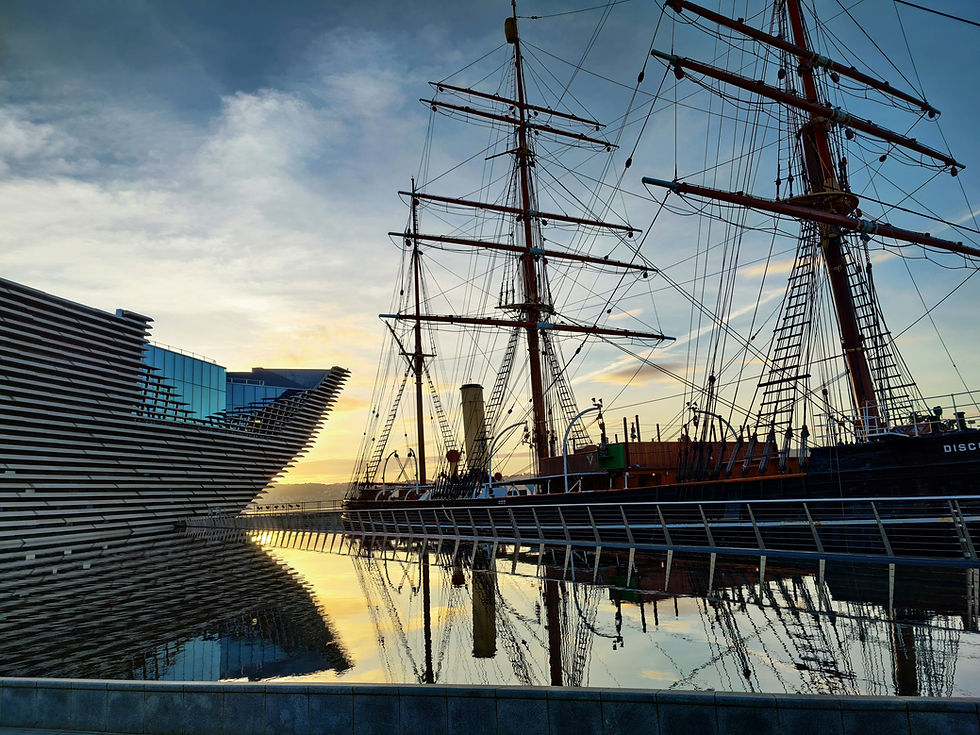 The modern geometric architecture of the V&A Dundee design museum alongside the historic wooden hull of the RRS Discovery ship on the River Tay.