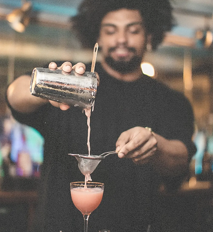 Smiling bartender straining a cocktail into a coupe glass.