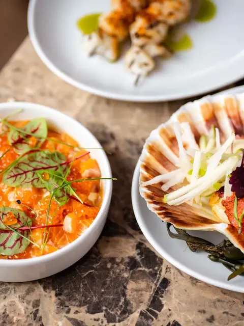 Scallop and salmon dishes served on elegant plates as part of Above's seasonal seafood menu.