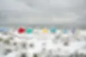 Snow-covered beach huts in different colours beside the sea under a cloudy winter sky.