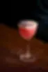 Pink cocktail with a foamy top and dried lavender garnish served in a stemmed glass.