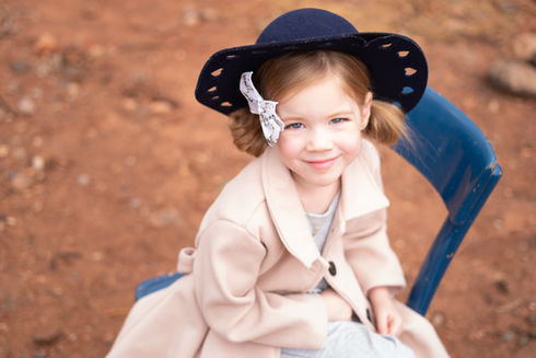 Young girl smiles while wearing a hat and coat, sitting on chair