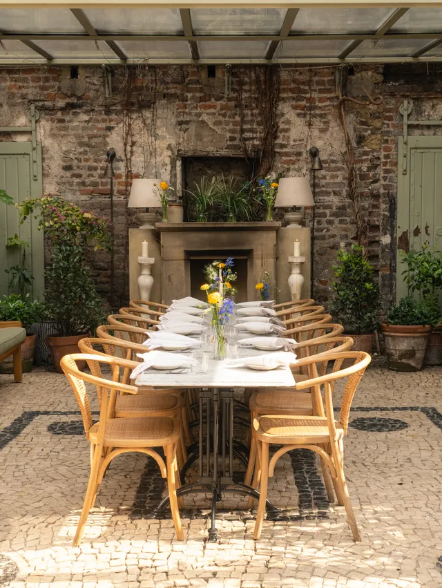 An outdoor dining area at Luca - Clerkenwell, with wooden tables and chairs set against a brick wall backdrop.