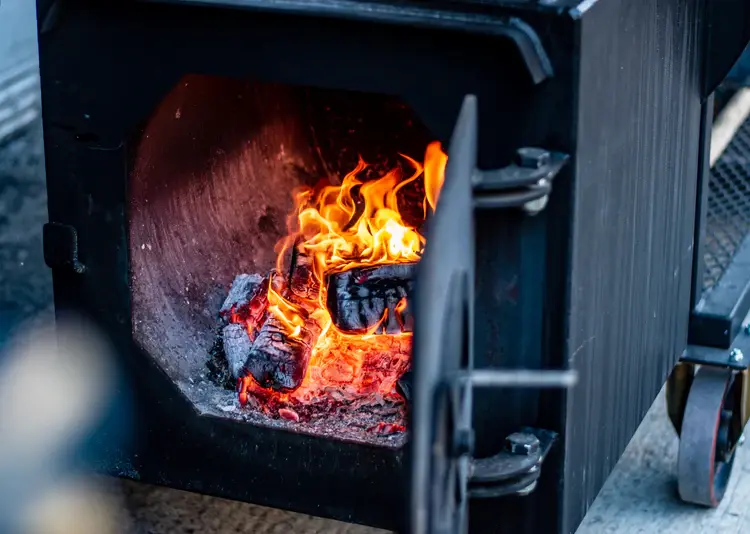 A fiery open oven with glowing coals and flames, used for cooking, at From The Ashes - Hackney.