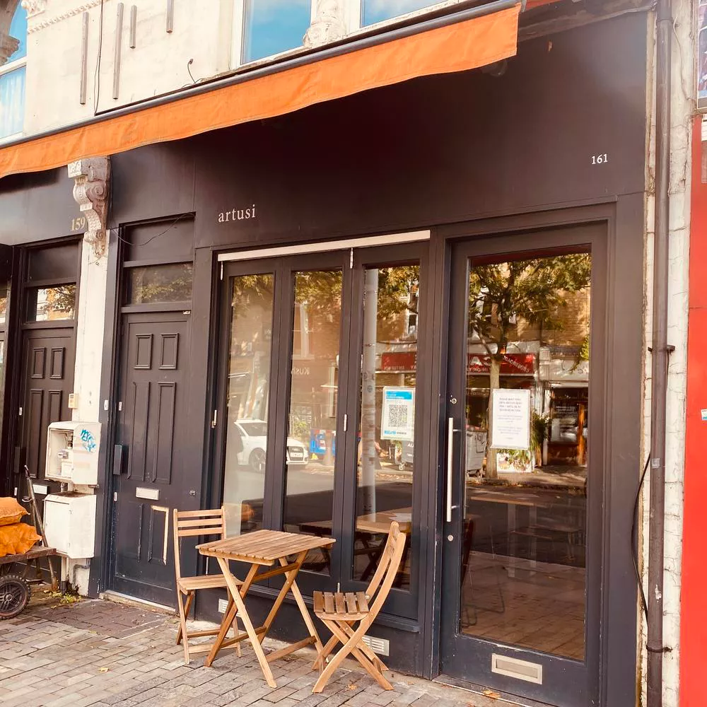The exterior of Artusi - Peckham & Soho, showing a charming storefront with outdoor seating.