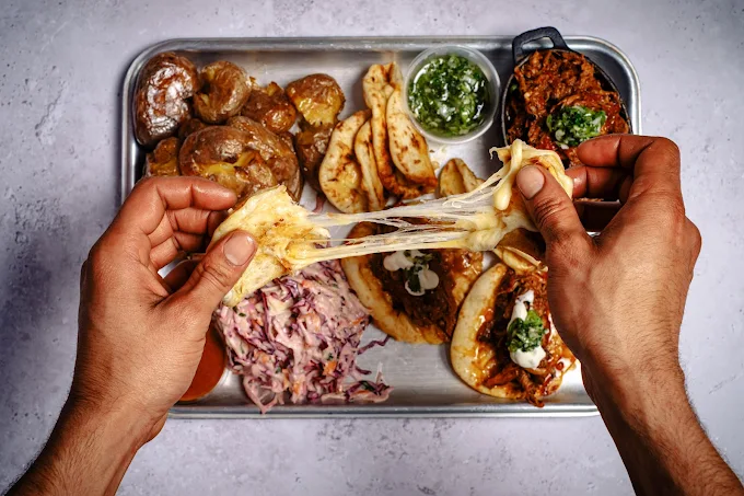 A collage of images from Cue Point at Ely’s Yard - Brick Lane, featuring a British-Algerian BBQ with smoked lamb, ribs, and a burger, with a hand preparing food and various dishes on a table.