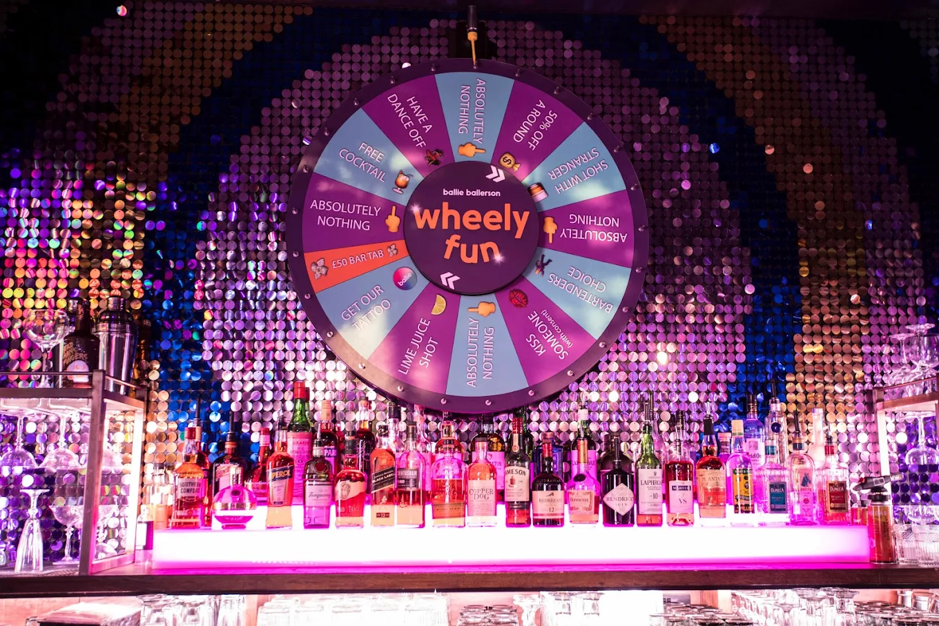 Bar area at Ballie Ballerson with a brightly lit prize wheel above rows of bottles.
