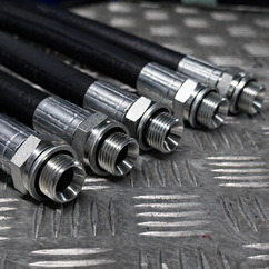 A range of hydraulic hoses with hydraulic fittings aligned on an industrial steel tread plate workbench.