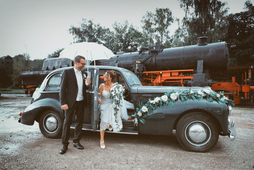 Bräutigam holt die Braut mit einem Oldtimer am Bahnhof nahe Freiburg im Breisgau ab, historische Lokomotive, emotionale Hochzeitsfotografie