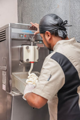 Man in a commercial kitchen dispensing ice cream from a soft-serve machine.
