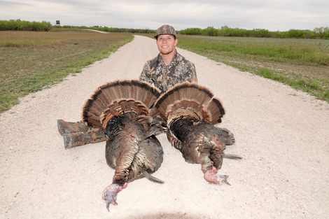 A hunter sitting on the ground next two his two turkeys