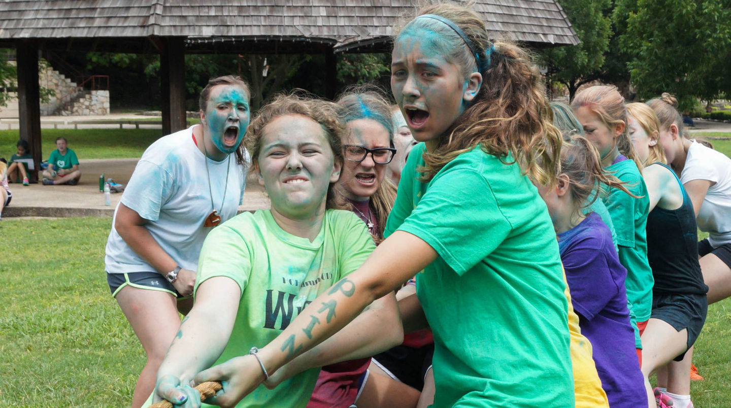 Girls with painted faces work together pulling on a rope in a game of tug.