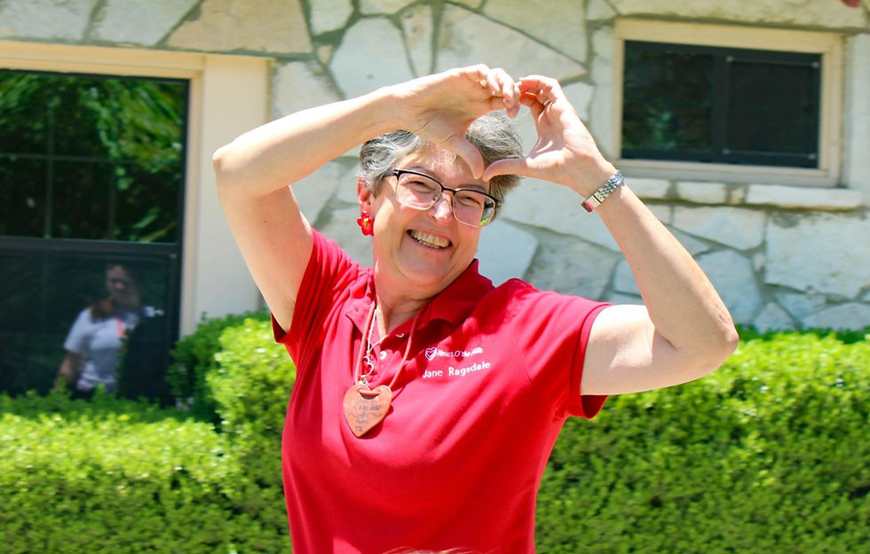 A smiling woman in a red tee shirt holding a strawberry up to the camera.