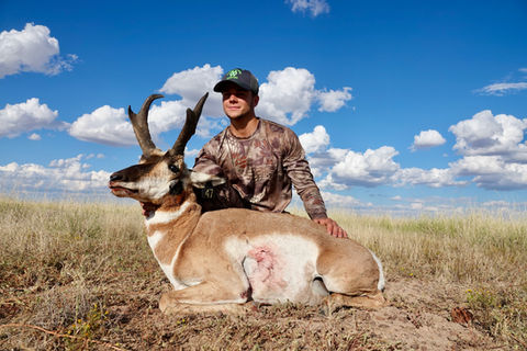 A hunter kneels next to his trophy pronghorn on a bright Texas day.