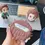 Thumbnail: Hand holding Tanjiro Kamado AirPods case with two figures on laptop background