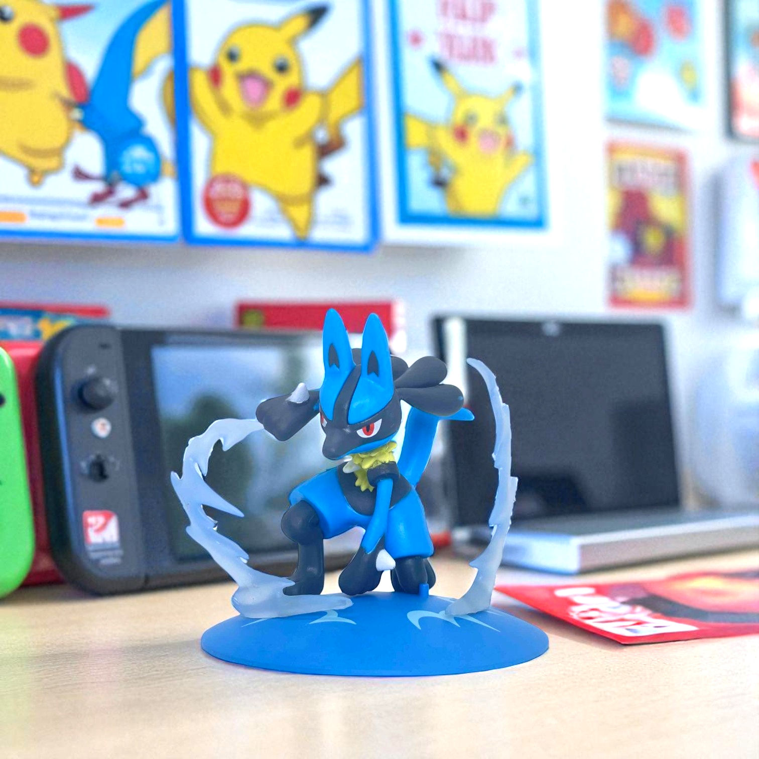 Lucario figurine on display with Nintendo Switch and Pokemon cards in background.