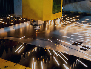 Yellow laser cutter sparks fly as it cuts metal in an industrial setting, creating a dynamic and intense atmosphere.