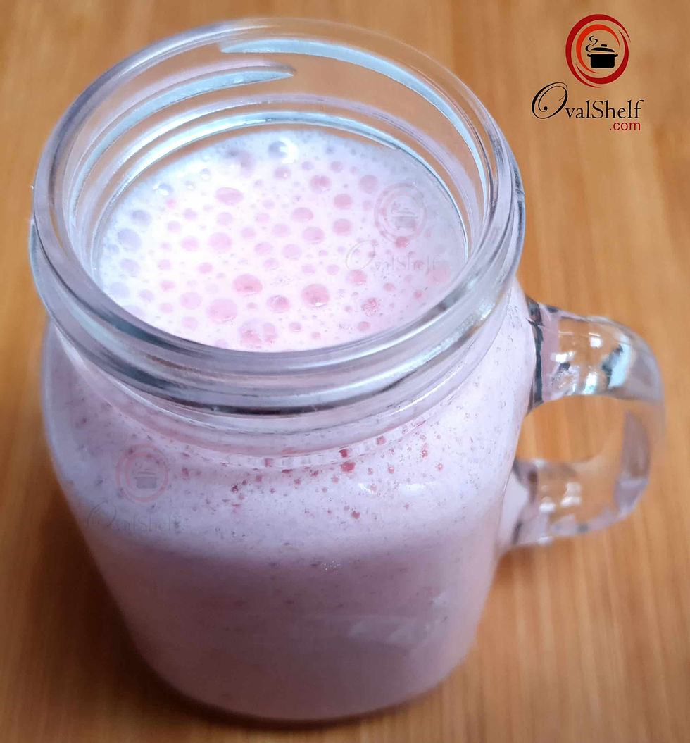 A glass jar filled with frothy pink strawberry ice cream milkshake on a wooden surface.