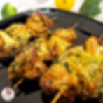 Air Fried Malai Broccoli skewers on a black plate, with charred edges and visible seasoning. Background includes a lemon and broccoli florets.
