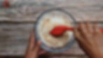 How to make Sabudana Khichdi - Method 6 -Hands mixing sabudana, peanuts, salt, sugar in a glass bowl with a red spatula. Background is a rustic wooden surface.