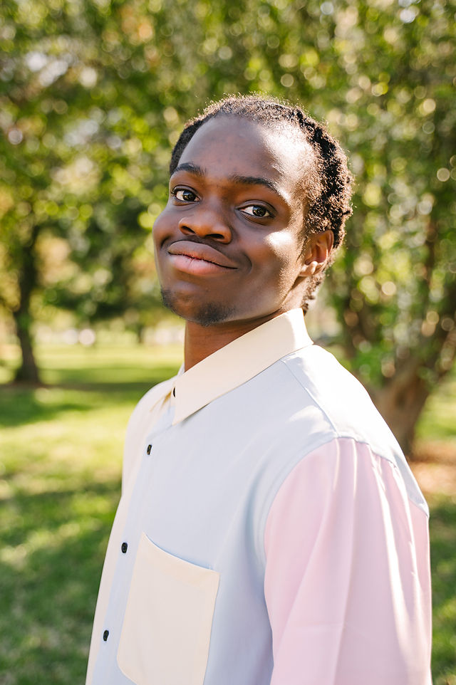 Young man wearing a pastel shirt posing at a park full of trees