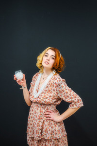 female high school senior with red hair posing in studio with black background wearing pearls and a warm floral dress