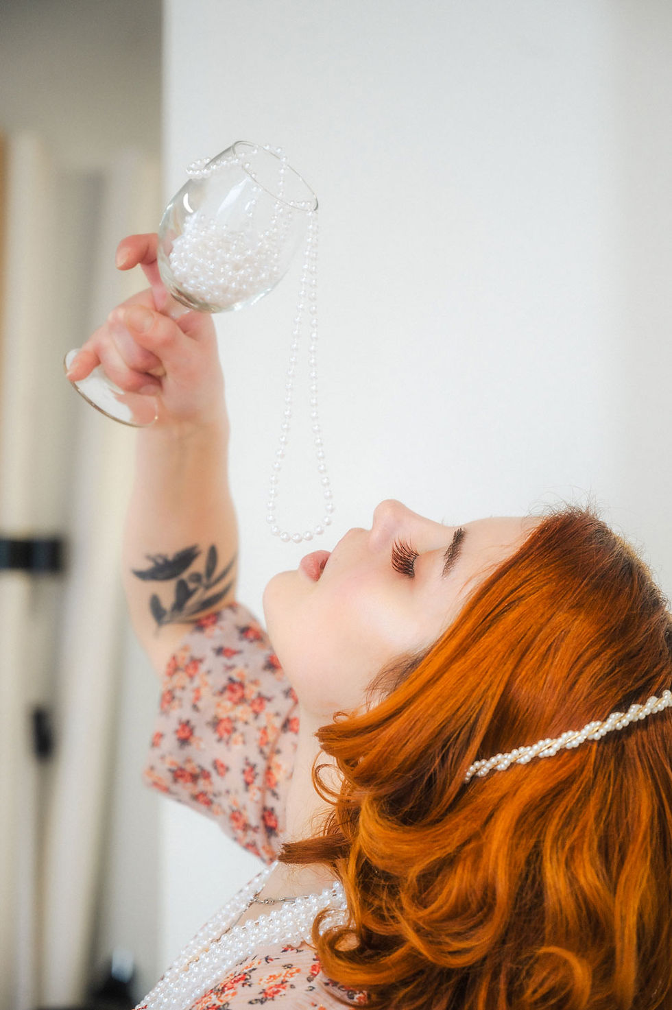 female high school senior with red hair posing in studio with white background wearing pearls and a warm floral dress