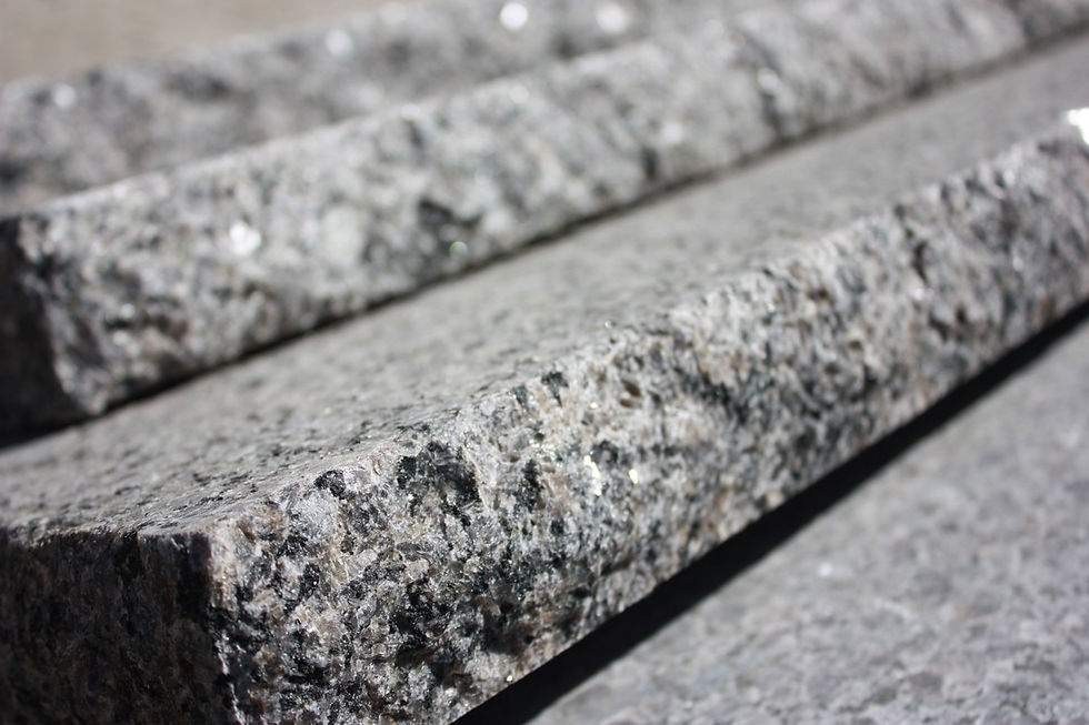 A close up of Caledonia granite treads. The granite is taupe with black flecks, The front edge is chiseled to appear natural