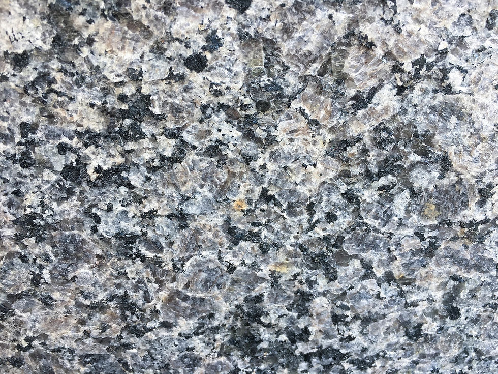 A color swatch of Caledonia granite natural stone. The granite is taupe grey with peach and black flecks.