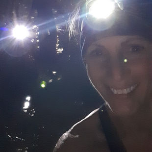 A woman with a head torch beside a loch at night