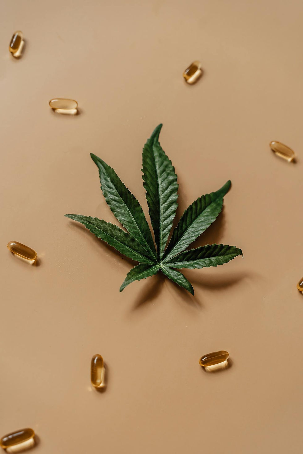 Cannabis leaf centered on a beige background, surrounded by scattered transparent capsules. The scene is calm and earthy.