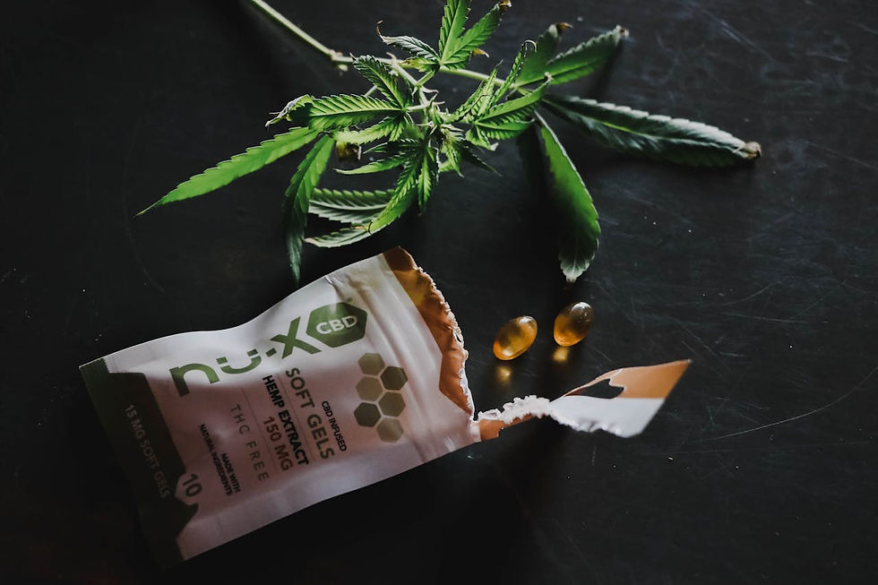 CBD soft gels and two capsules on a dark surface with a cannabis leaf above. Green and brown tones dominate the image.