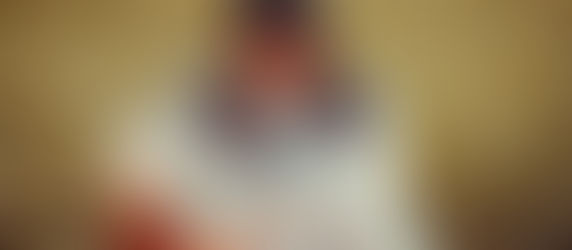 Man wearing glasses and a hat sits in tall grass, vaping. Smoke surrounds him, creating a serene, relaxed atmosphere.