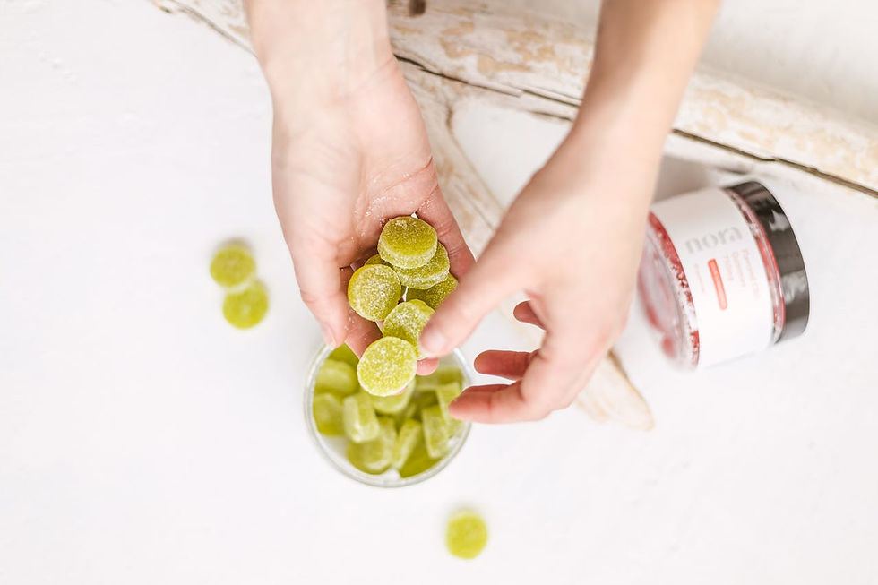Hands holding green sugared candies above a glass jar on a white surface. A product container with visible text "nora" is nearby.