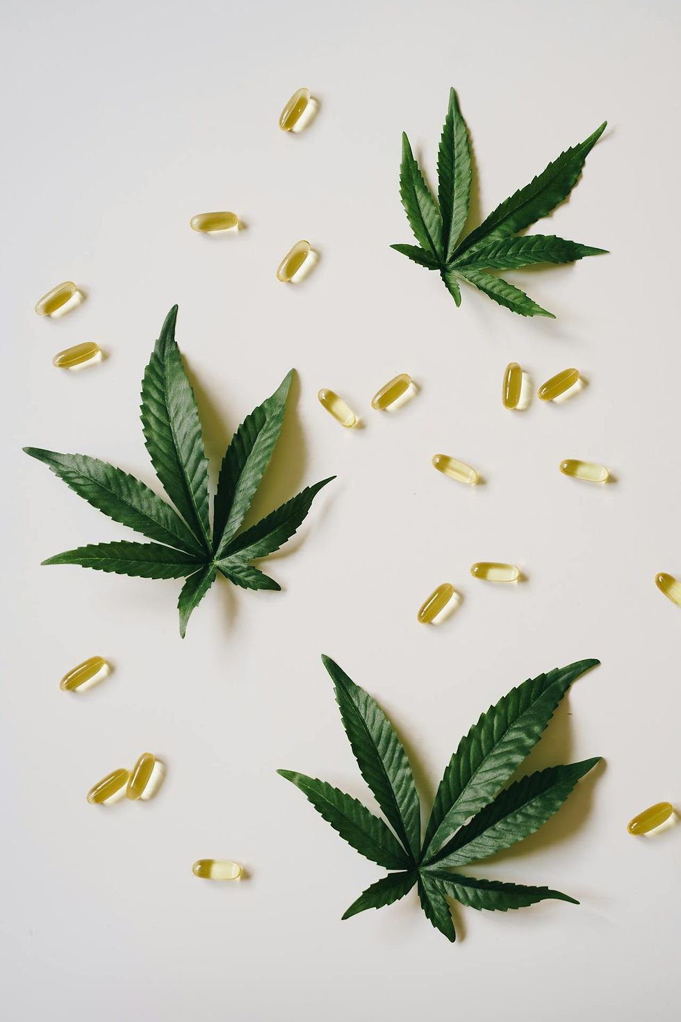 Cannabis leaves and yellow capsules scattered on a white background, creating a natural and serene composition.