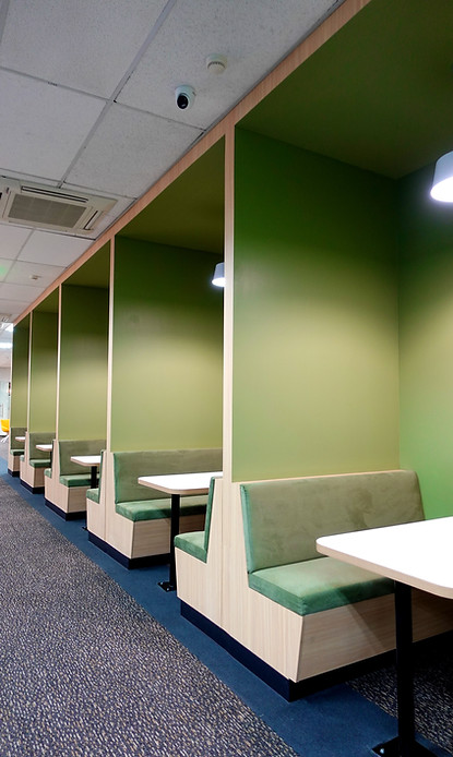 A spacious hallway lined with green couches and tables for seating