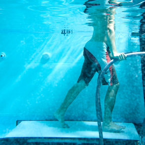 Person walking underwater on treadmill, holding a curved bar. Clear water with light reflections, blue and white color scheme.