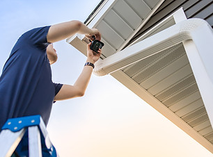 Technician on ladder installing and adjusting wireless security video camera underneath a
