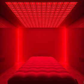 Empty padded massage bed under large overhead red light panel, distant view. Massive recta