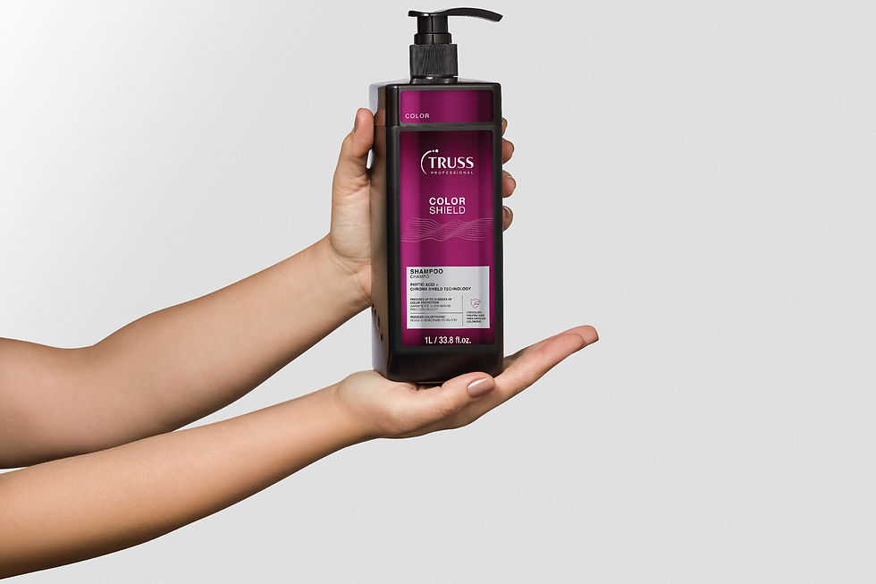 Mãos seguram frasco de shampoo TRUSS Color Shield roxo/preto, com texto visível, em fundo branco minimalista.