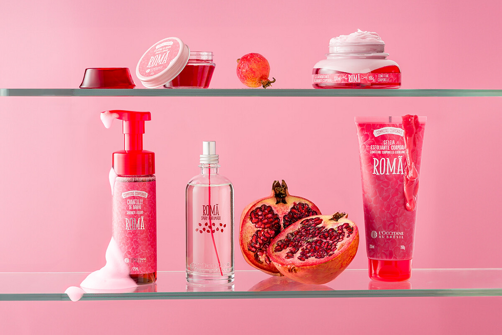 Produtos de romã rosa em prateleiras de vidro, com gel, spray, creme e romã cortada; rótulos ROMÃ.