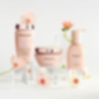Frascos rosa da Kérastase Gloss Absolu com flores delicadas sobre fundo branco, em composição minimalista.