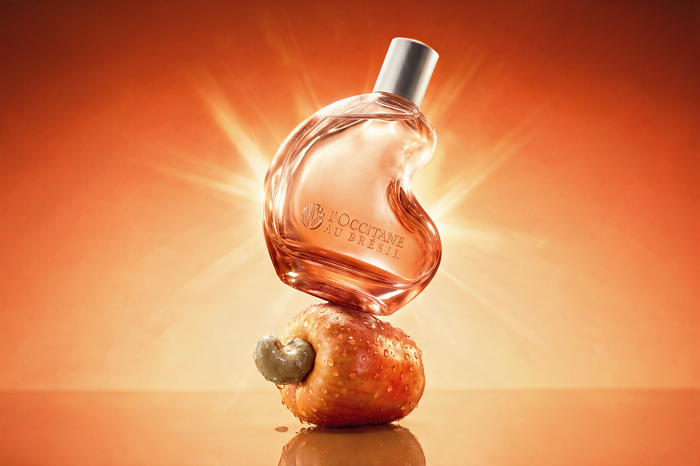 Frasco de perfume L’Occitane au Brésil sobre um caju laranja, com fundo dourado radiante e clima luxuoso.