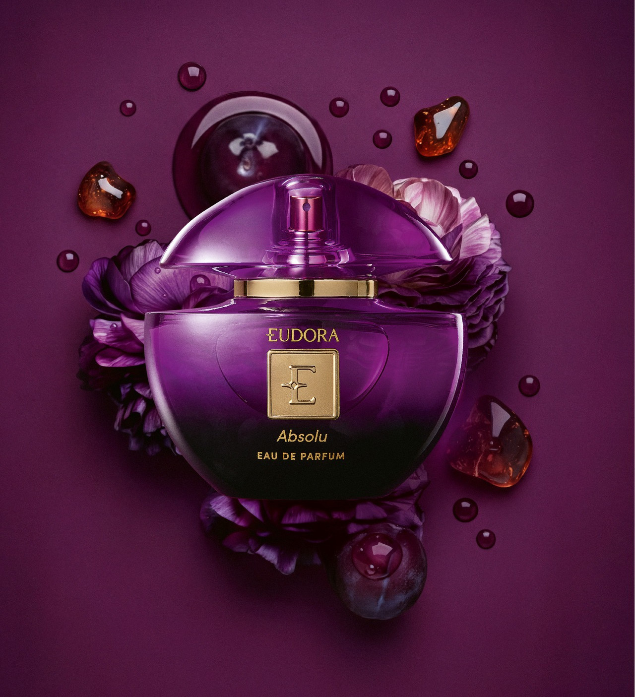 Frasco roxo de perfume Eudora Absolu sobre flores roxas, com gotas brilhantes em fundo lilás escuro.