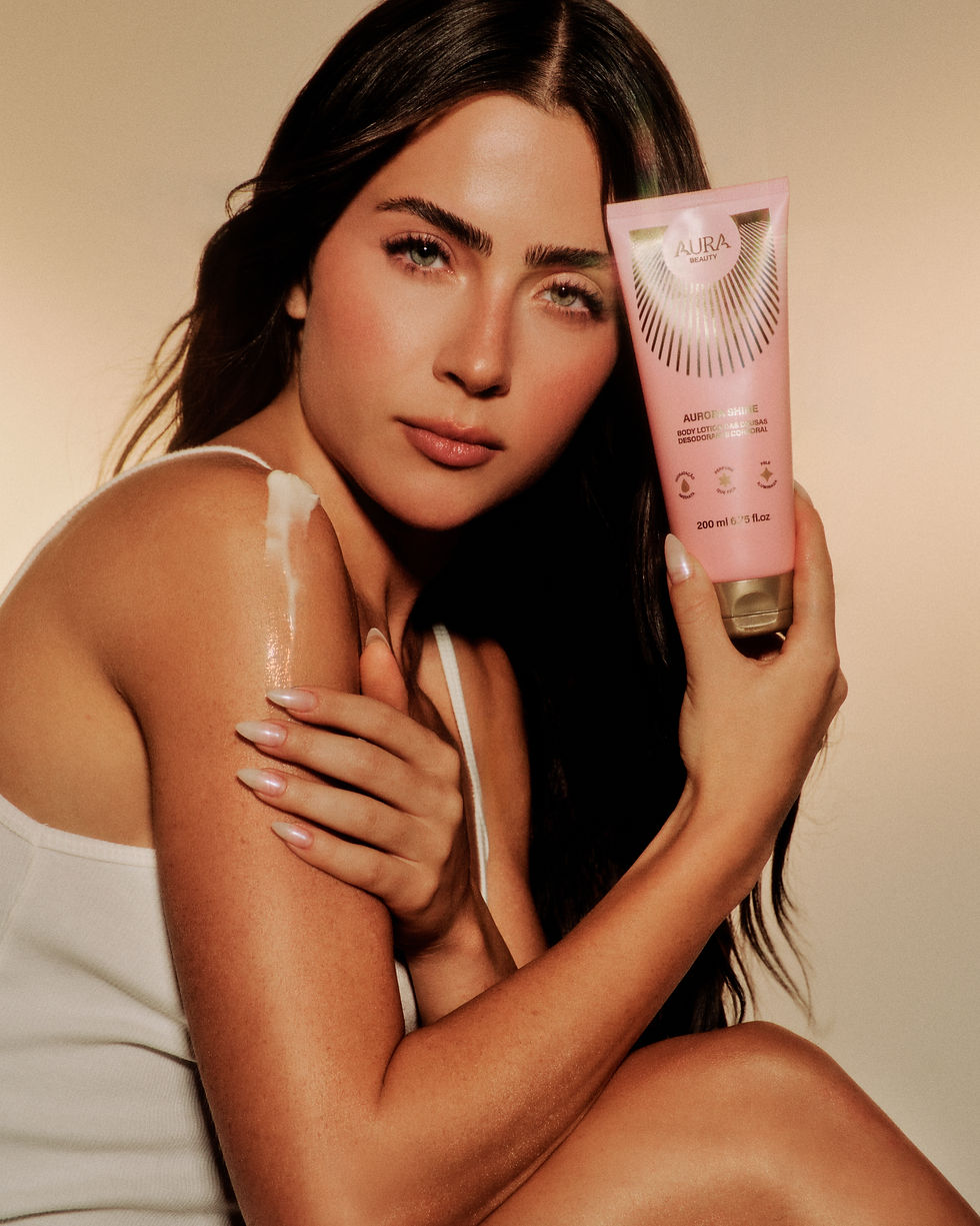 Mulher posa com frasco rosa Aura Beauty; creme no ombro e expressão serena em fundo bege.