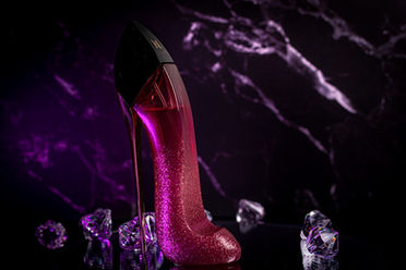 Luxury editorial perfume photo of Carolina Herrera Good Girl Glam in a sparkling pink stiletto bottle with purple lighting and crystal accents.